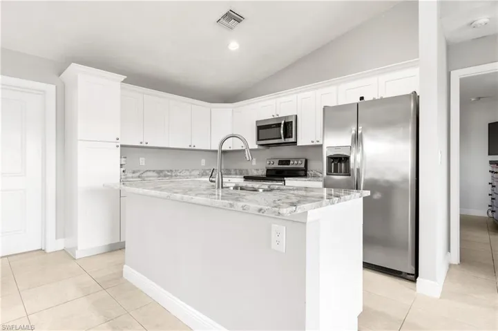 Kitchen with white cabinetry, stainless steel appliances, vaulted ceiling, a kitchen island with sink, and light tile patterned flooring
