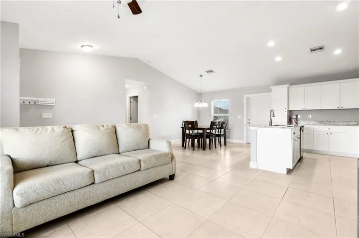 Living room featuring ceiling fan with notable chandelier, light tile patterned flooring, lofted ceiling, and sink