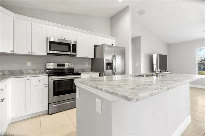 Kitchen with white cabinets, stainless steel appliances, lofted ceiling, and an island with sink