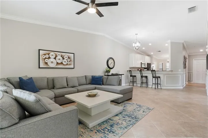 Living area with crown molding, vaulted ceiling, a chandelier, light tile patterned flooring, and recessed lighting