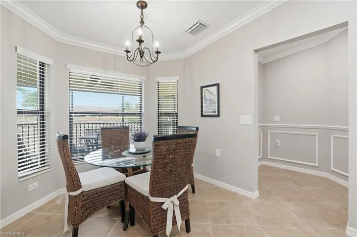 Dining area featuring light tile patterned floors, a decorative wall, a chandelier, wainscoting, and crown molding