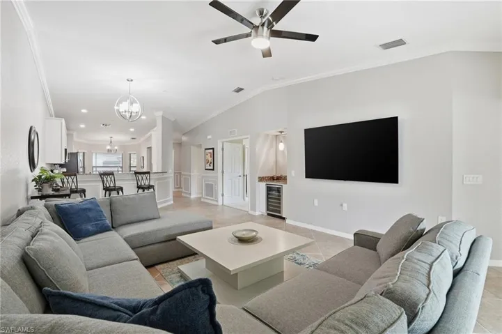 Living room with crown molding, vaulted ceiling, a chandelier, light tile patterned flooring, and ceiling fan