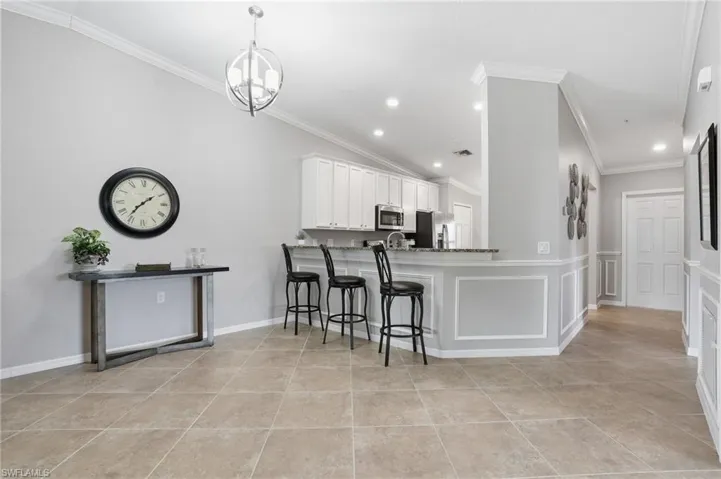 Kitchen featuring a kitchen breakfast bar, white cabinetry, a peninsula, ornamental molding, and stainless steel appliances