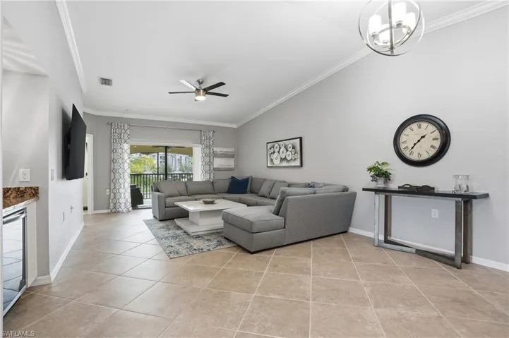Living room with ornamental molding, a ceiling fan, light tile patterned floors, and beverage cooler