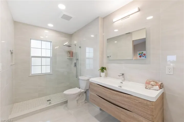 Bathroom featuring vanity, a tile shower, tile walls, and toilet