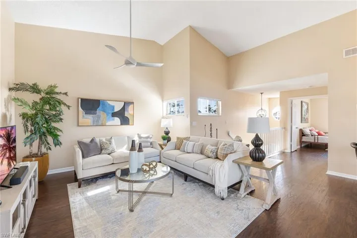 Living room with dark hardwood / wood-style flooring, high vaulted ceiling, and ceiling fan