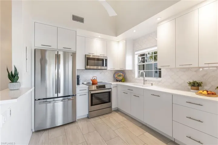 Kitchen featuring sink, backsplash, stainless steel appliances, and white cabinets