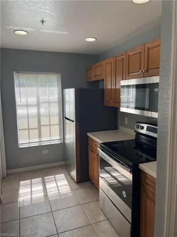 Kitchen featuring appliances with stainless steel finishes, light tile patterned floors, and a textured ceiling