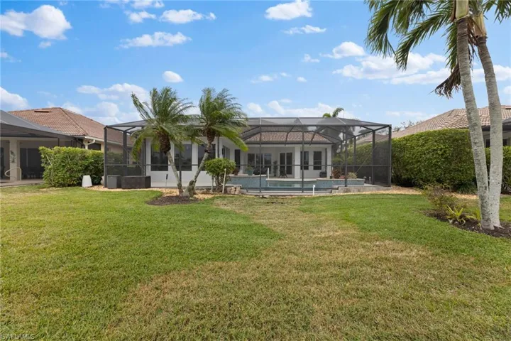 Rear view of home featuring a lanai, a landscaped lawn, and an outdoor pool and spa