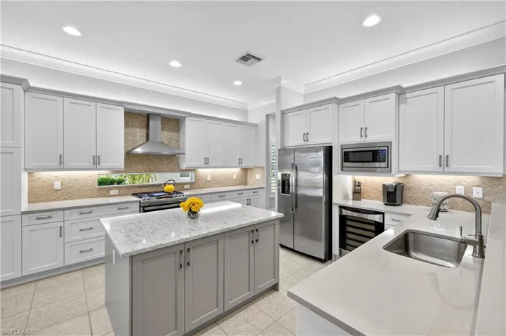 Kitchen featuring backsplash, gray cabinets, light stone countertops, wall chimney range hood, and stainless steel appliances