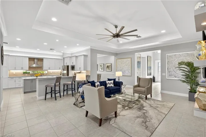 Living area with a tray ceiling, crown molding, light tile patterned floors, recessed lighting, and a ceiling fan