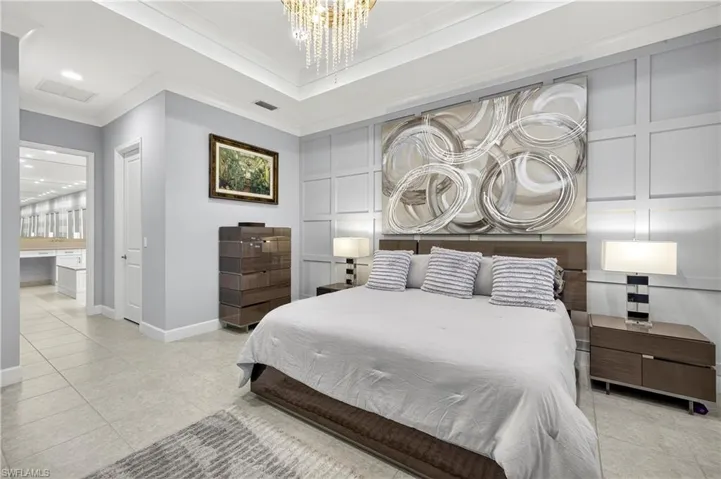 Bedroom featuring ornamental molding, a chandelier, light tile patterned floors, ensuite bathroom, and a tray ceiling