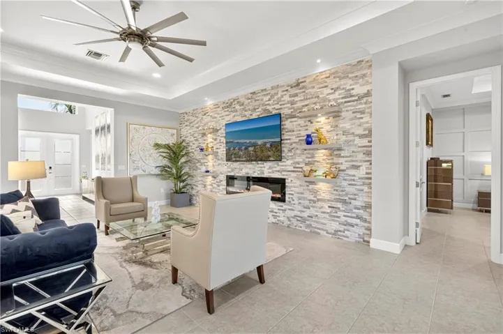 Living area with light tile patterned floors, french doors, a ceiling fan, a tray ceiling, and a fireplace