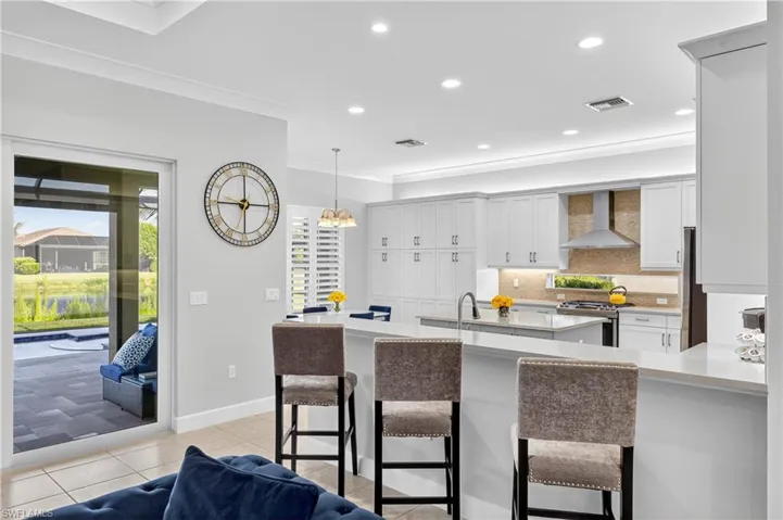 Kitchen featuring a kitchen bar, recessed lighting, tasteful backsplash, wall chimney exhaust hood, and white cabinets