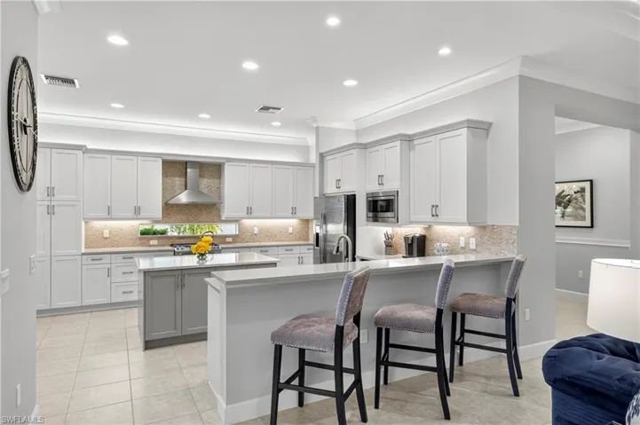Kitchen with a kitchen bar, backsplash, a peninsula, recessed lighting, and white cabinetry