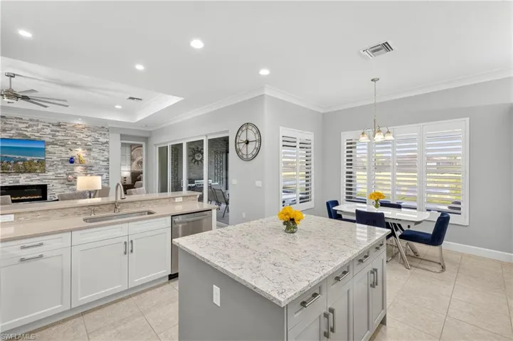 Kitchen with ornamental molding, hanging light fixtures, a tile fireplace, light stone countertops, and light tile patterned floors
