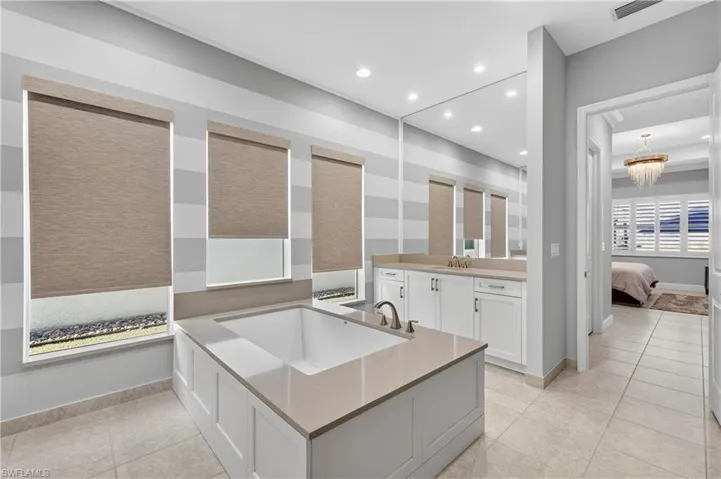 Ensuite bathroom with light tile patterned floors, vanity, a garden tub, recessed lighting, and a chandelier