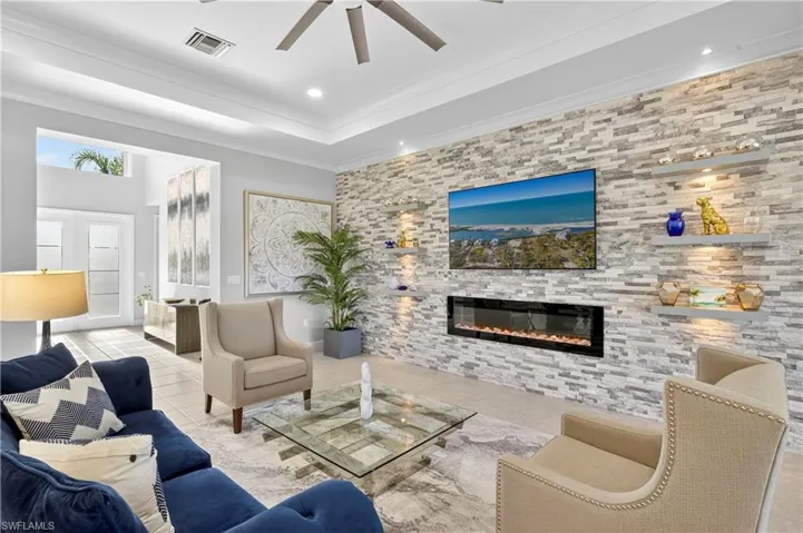 Tiled living area featuring a large fireplace, a ceiling fan, ornamental molding, recessed lighting, and a raised ceiling
