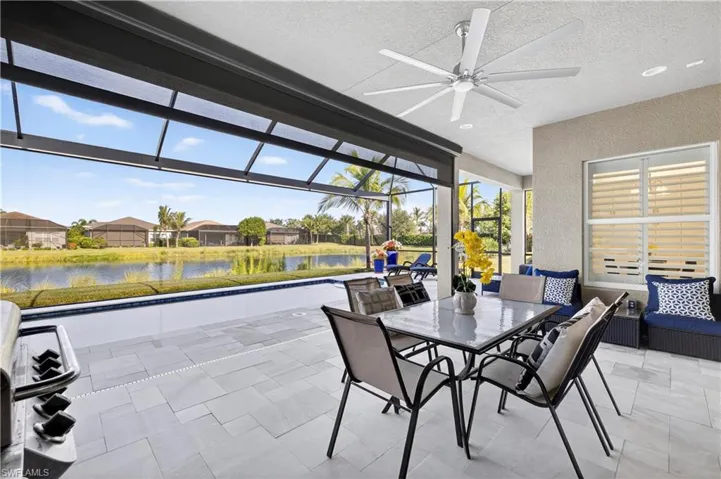 View of patio with glass enclosure, a sunroom, a water view, outdoor dining space, and a ceiling fan
