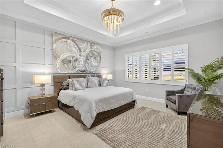 Bedroom with a raised ceiling, ornamental molding, a chandelier, and a decorative wall