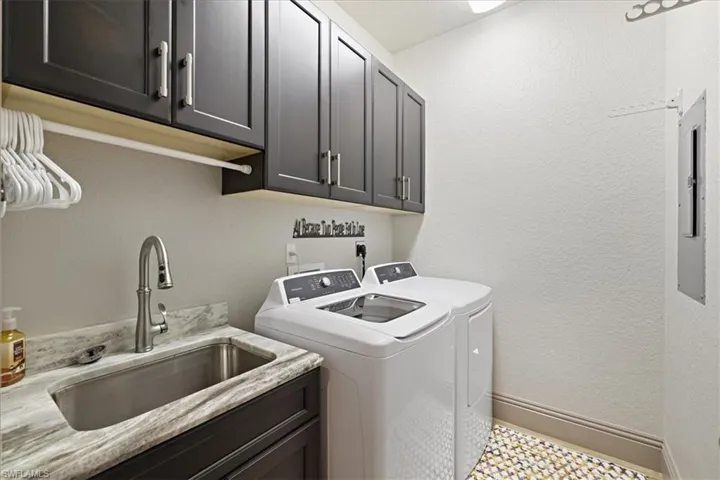 Washroom with a textured wall, washing machine and dryer, cabinet space, and electric panel