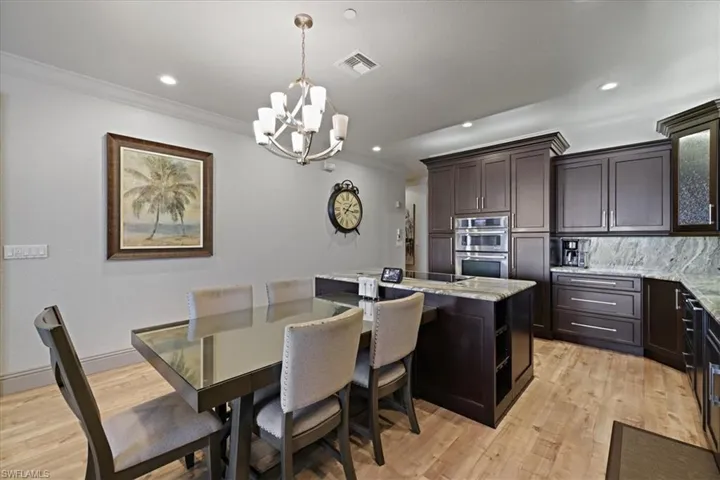 Kitchen featuring light stone counters, a kitchen island, hanging light fixtures, decorative backsplash, and dark brown cabinetry