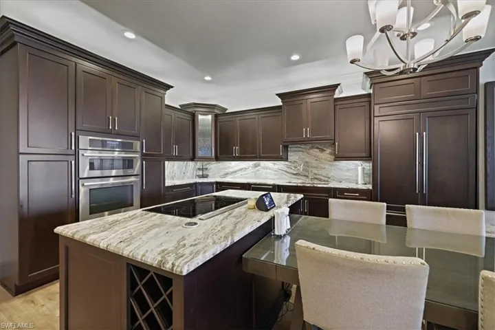 Kitchen with dark brown cabinets, decorative light fixtures, glass insert cabinets, double oven, and light stone counters