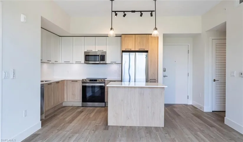 Kitchen featuring decorative backsplash, light countertops, light wood-style floors, and stainless steel appliances