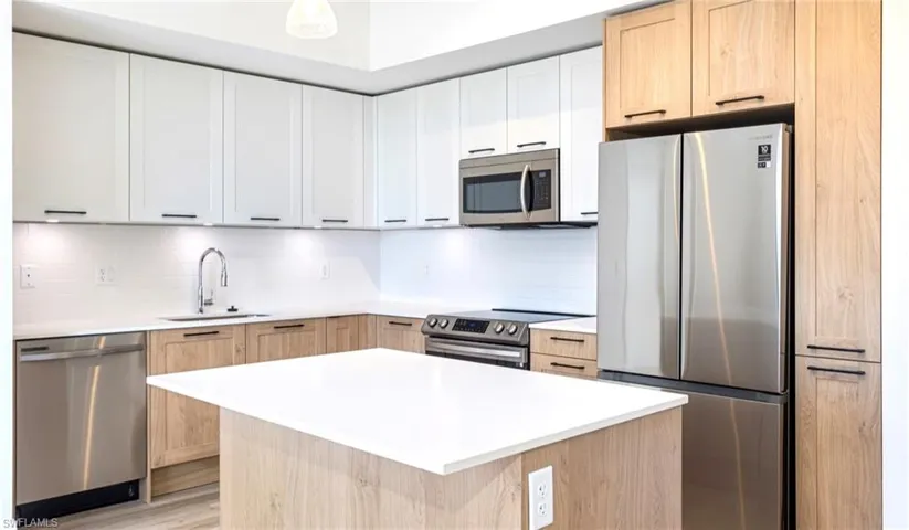 Kitchen with decorative backsplash, light countertops, appliances with stainless steel finishes, and a sink