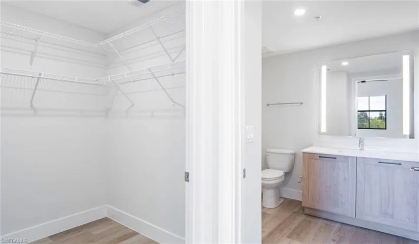 Bathroom with vanity, wood finished floors, baseboards, a spacious closet, and toilet