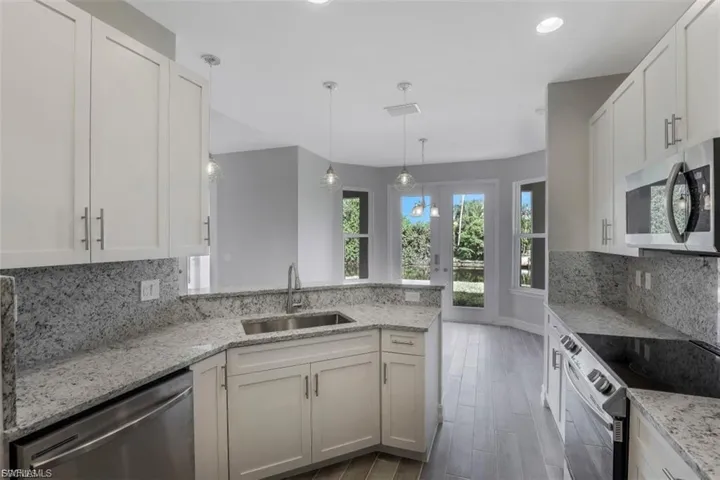 Kitchen with backsplash, a peninsula, stainless steel appliances, and light stone counters