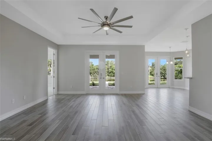 Unfurnished living room with french doors, ceiling fan, a raised ceiling, and wood finished floors