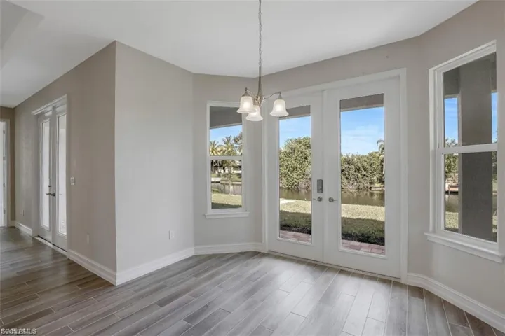 Unfurnished dining area featuring light wood-style flooring, suspended lighting, french doors, and a water view