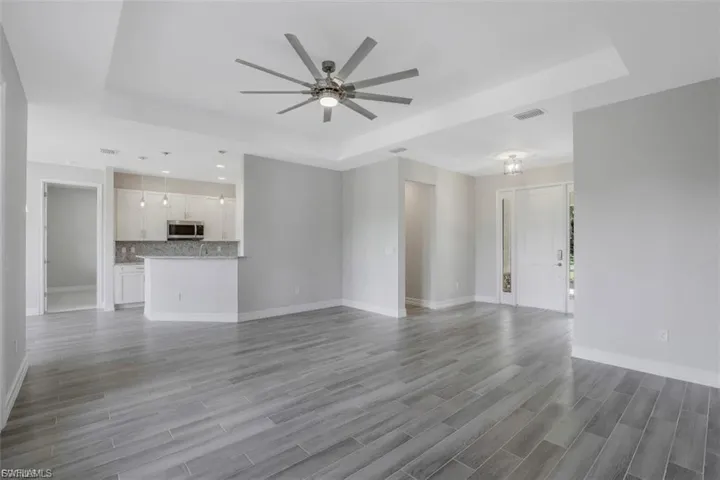Unfurnished living room with a raised ceiling, ceiling fan, and wood tiled floors