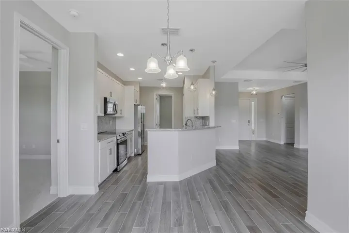 Kitchen featuring stainless steel appliances, wood finish floors, light stone counters, white cabinets, and hanging lights