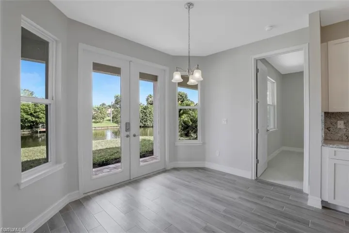 Unfurnished dining area featuring wood finish floors, hanging lights, a water view, and french doors