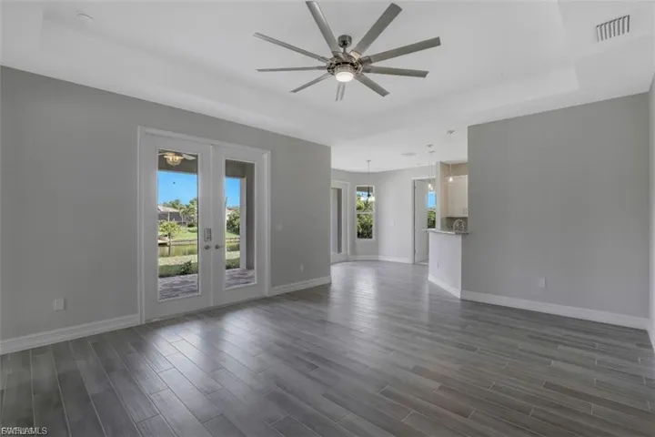 Unfurnished living room featuring a raised ceiling, ceiling fan, and dark wood-style floors