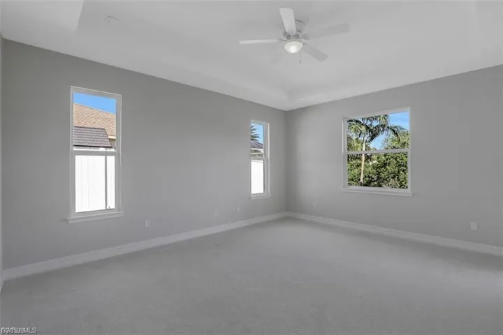 Carpeted spare room featuring a raised ceiling and ceiling fan