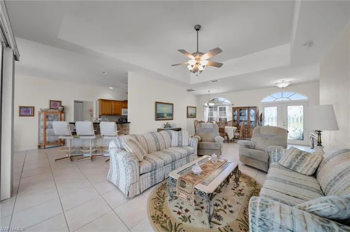 Living area featuring a tray ceiling, light tile patterned flooring, ceiling fan, french doors, and baseboards