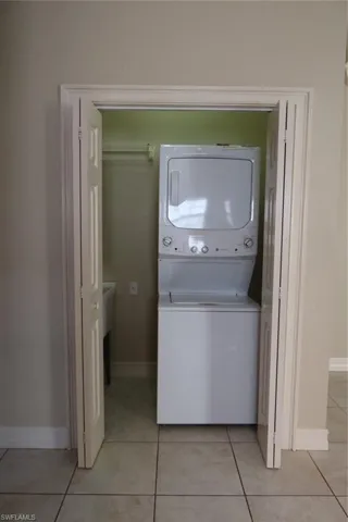Dedicated laundry closet featuring a white stacked washer and dryer unit, bi-fold doors, utility sink, and tile flooring