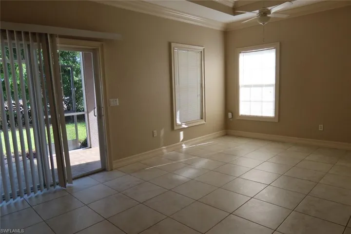 Spacious room featuring neutral tile flooring, crown molding, a tray ceiling with a ceiling fan, and multiple windows providing ample natural light