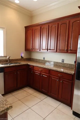 Kitchen featuring extensive cherry wood cabinetry, granite countertops, stainless steel sink, tiled flooring, and crown molding