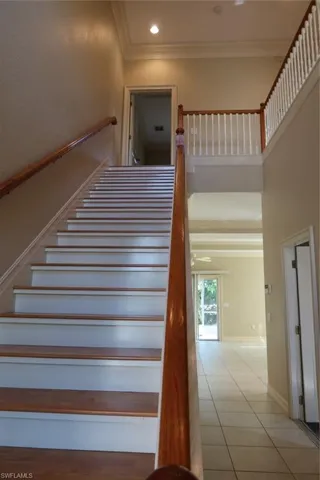 Two-story foyer featuring a wood-finish staircase with white risers, wood handrails, a second-story landing with white balusters, crown molding, and recessed lighting