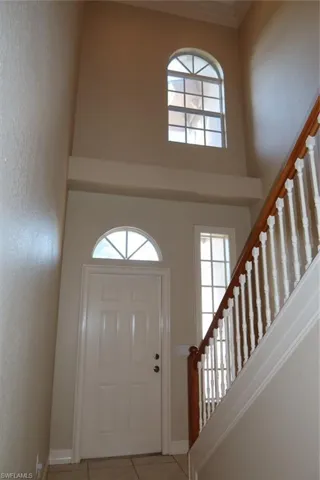 Two-story entry foyer featuring a paned entry door with an arched transom window, ceramic tile flooring, a staircase with wood handrails and white balusters, and a large arched window