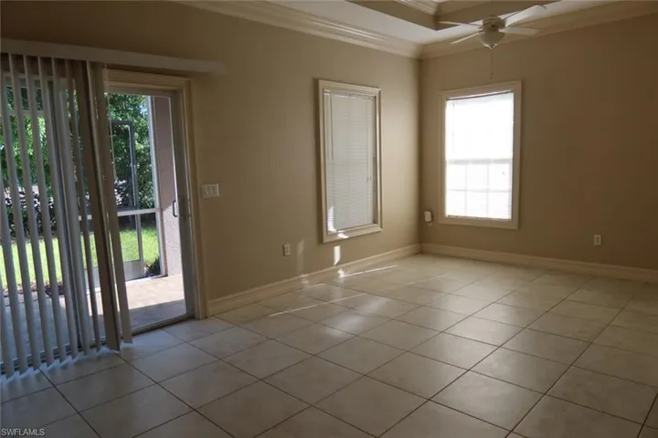 Spacious interior featuring neutral tone walls, square tile flooring, a tray ceiling with a fan, and windows