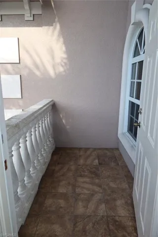 Tiled balcony featuring a decorative balustrade, stucco exterior, and an arched window with white framing