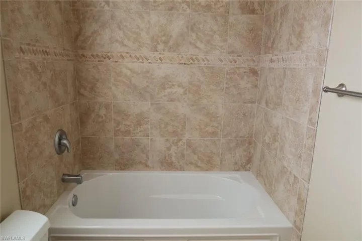 Bathtub surround featuring neutral-toned tile with a decorative accent band