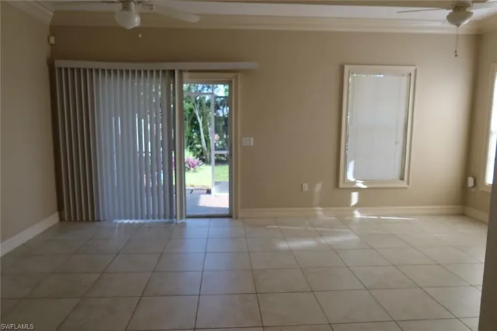 Spacious room featuring neutral-toned walls, light tile flooring, and crown molding