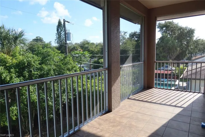 Screened balcony with tiled flooring, metal railings, and foliage beyond