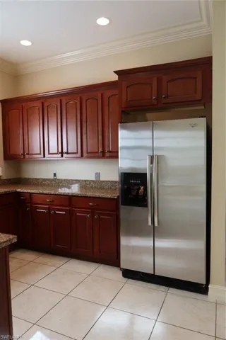 Kitchen featuring extensive wood cabinetry, speckled countertops, a stainless steel side-by-side refrigerator, recessed lighting, and tile flooring